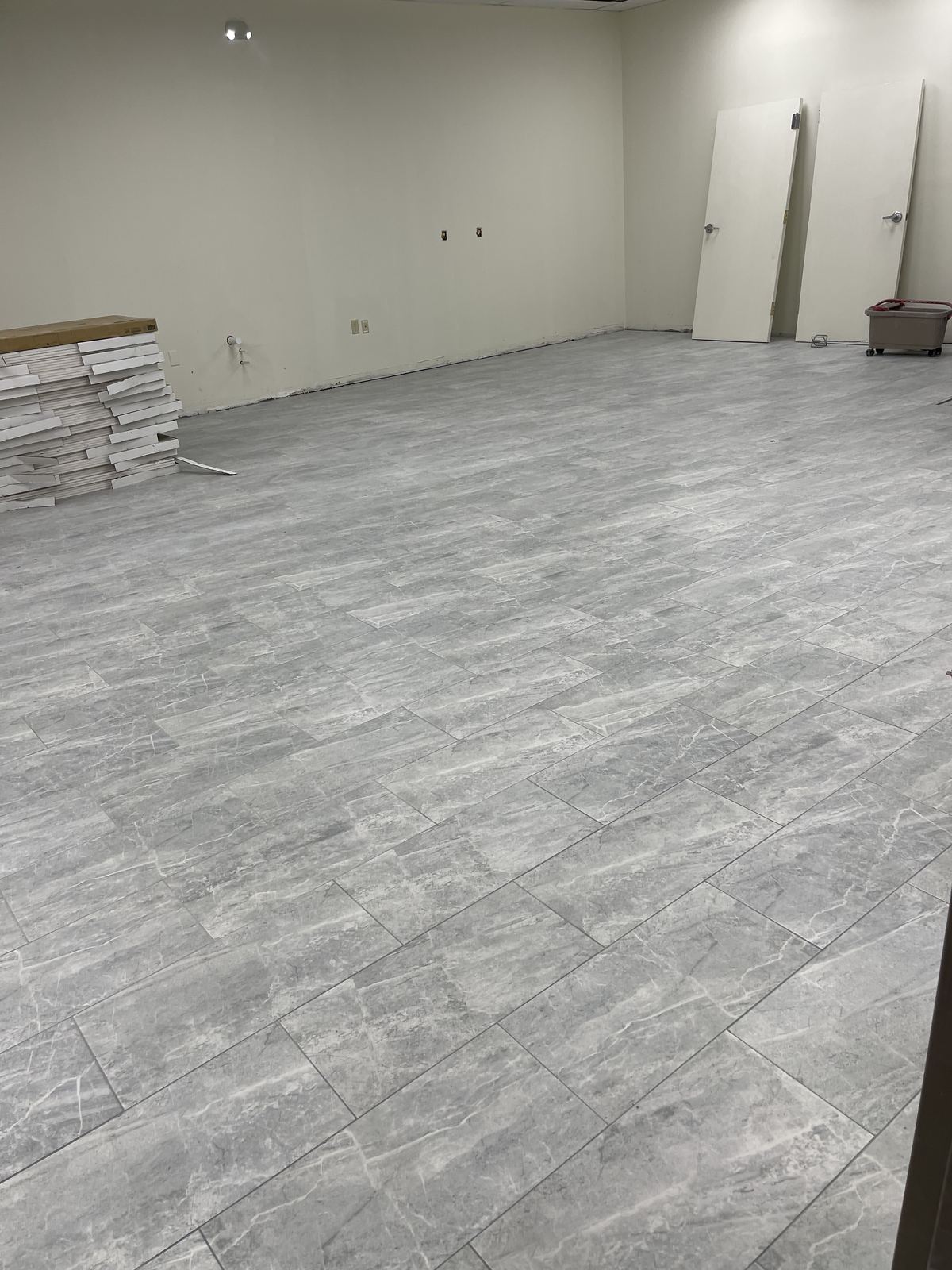 Finished large-format tile floor detail with doors staged nearby