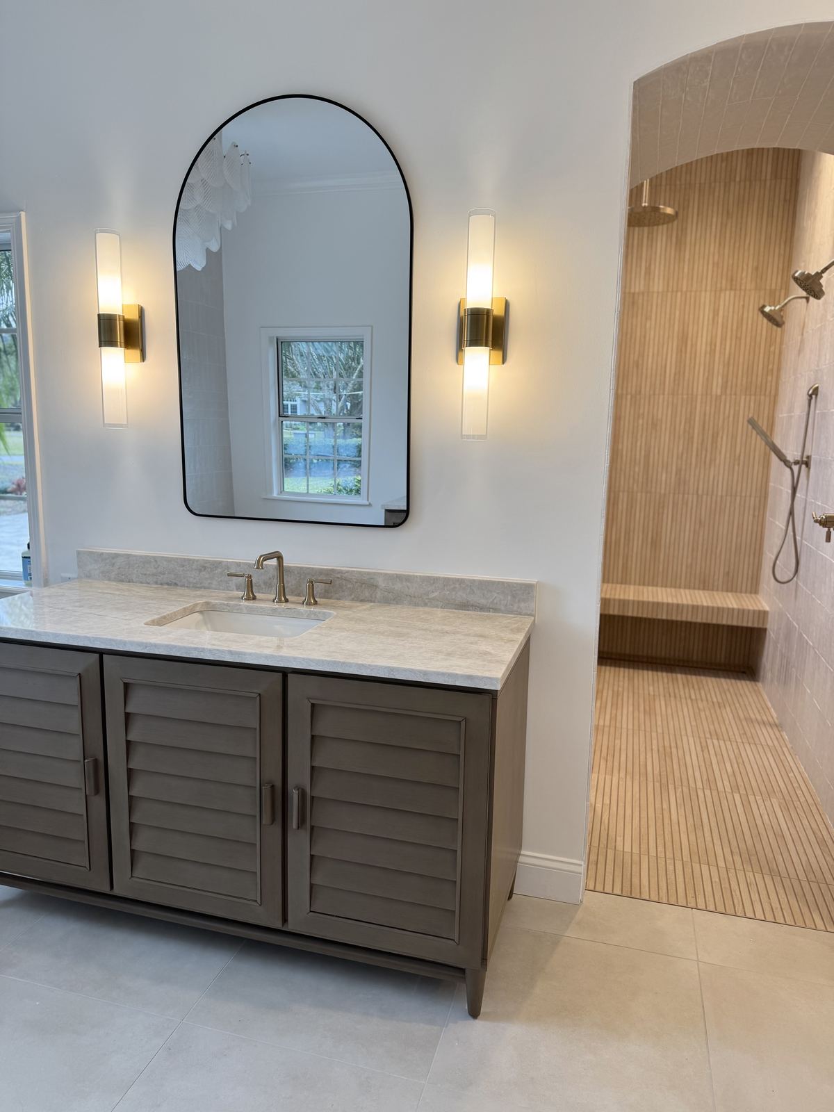 Finished vanity with arched mirror next to walk-in shower entry