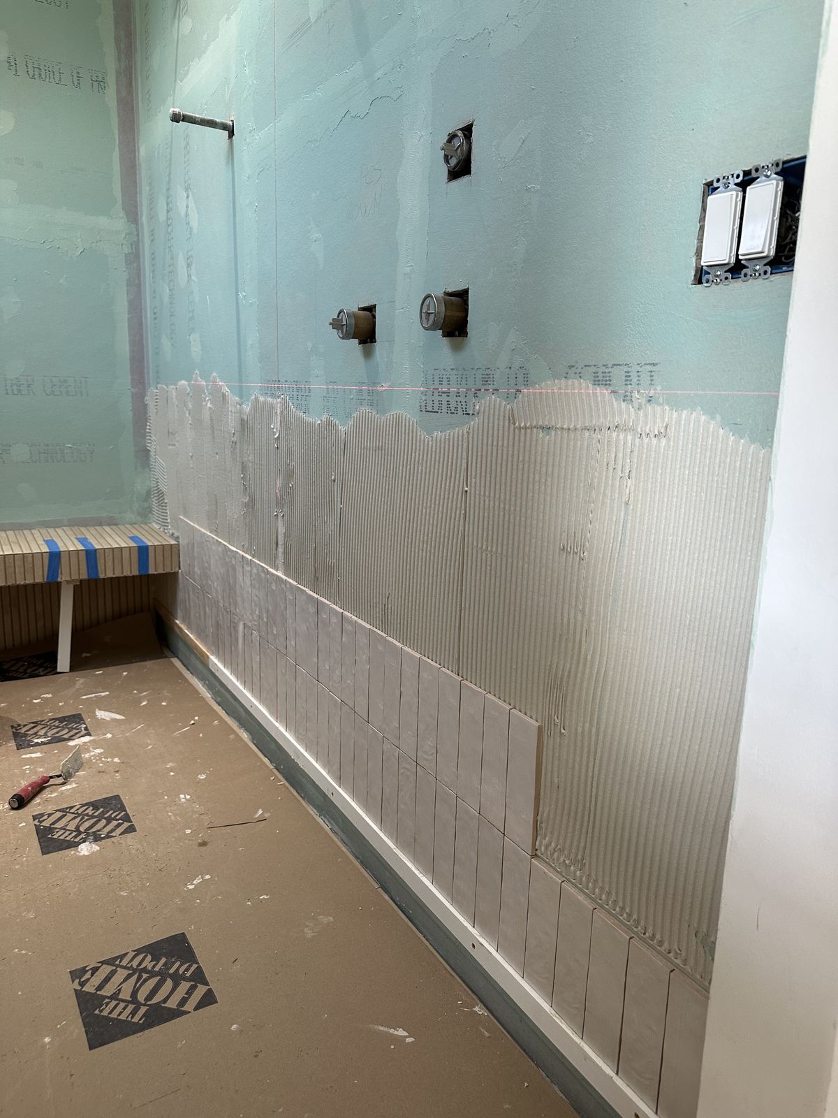 Shower tile installation in progress on green board
