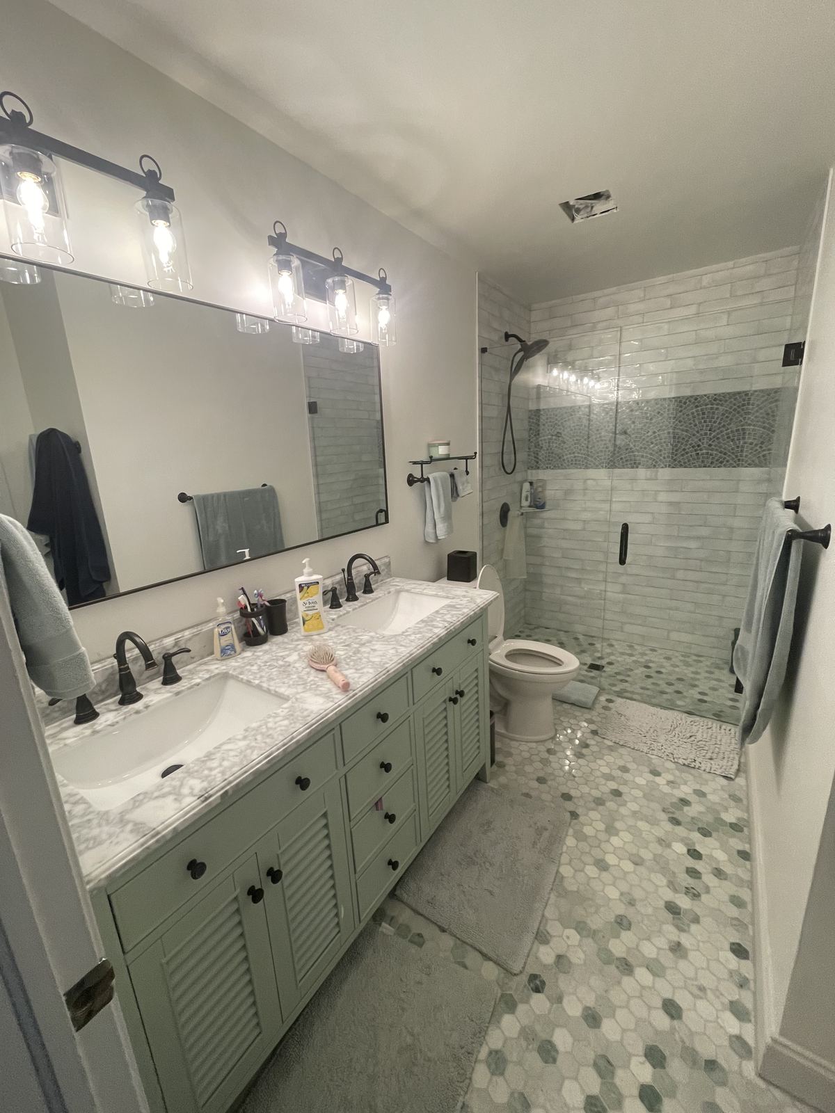 Finished bathroom with sage green dual vanity and glass shower