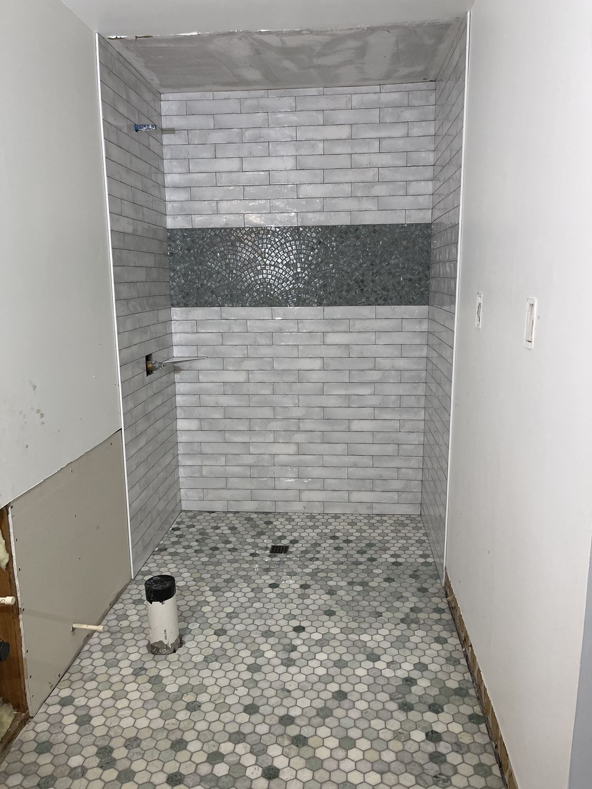 Finished walk-in shower with subway tile and glass mosaic band