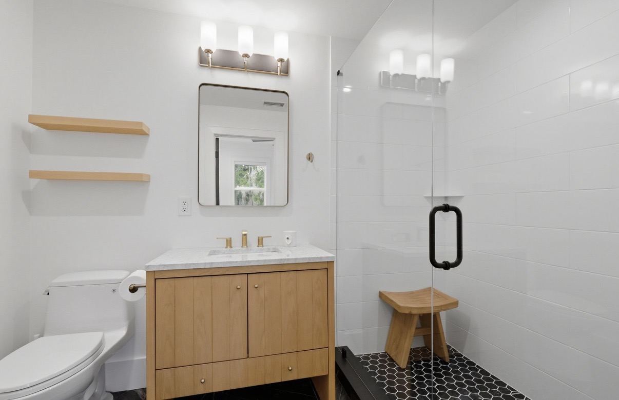 Finished bathroom with light wood vanity and black-and-white tiled walk-in shower