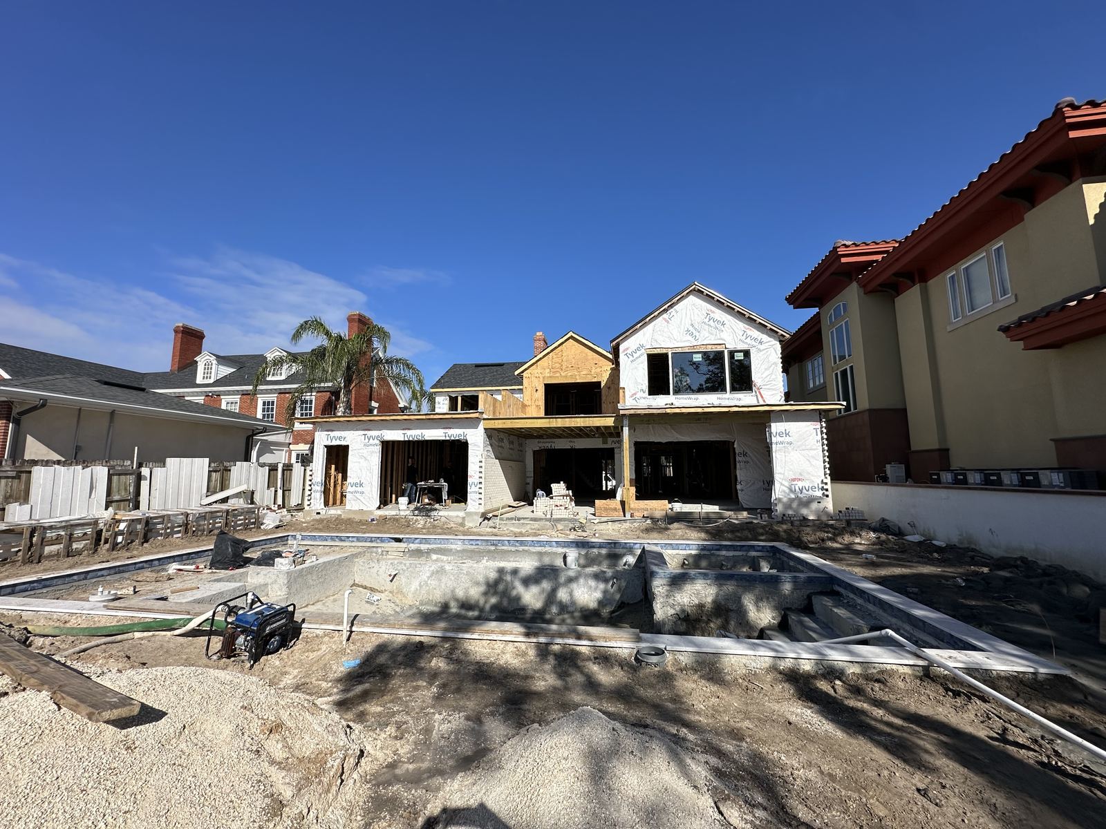 House wrapped in Tyvek with pool shell under construction
